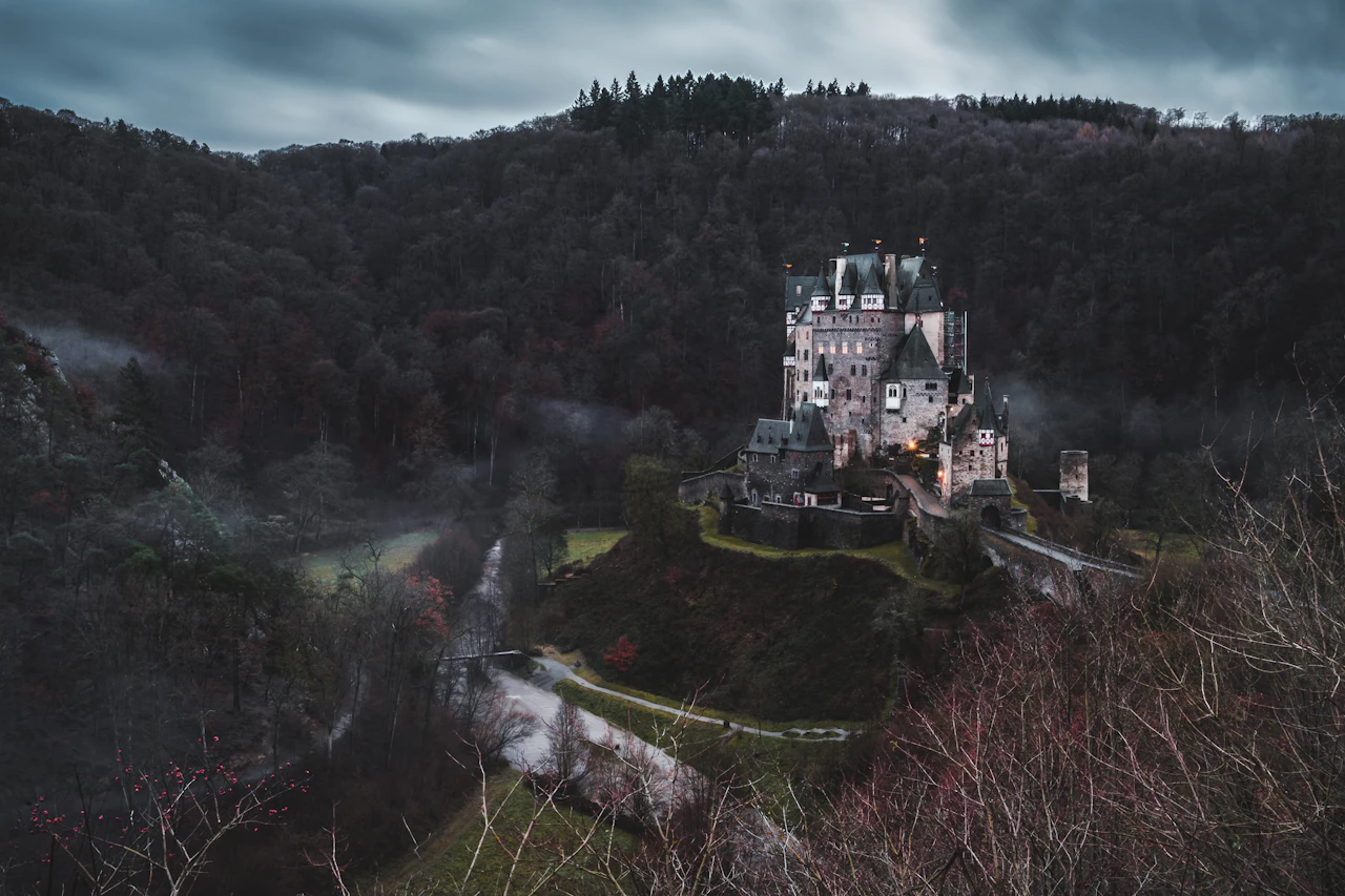 castello in pietra grigia circondato da alberi sotto un cielo coperto