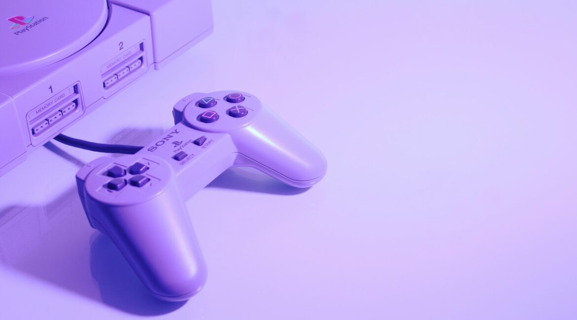 Prima PlayStation grigia con il suo controller a filo sotto una luce viola