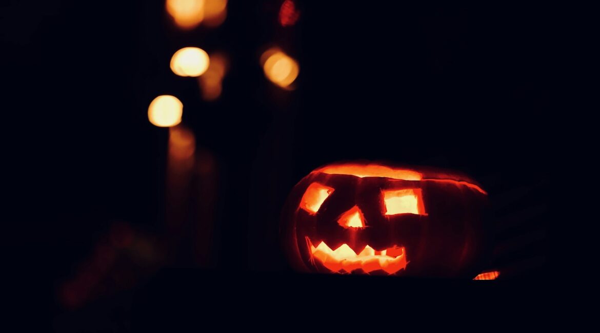 Zucca di Halloween intagliata e illuminata nel buio, con luci sfocate sullo sfondo