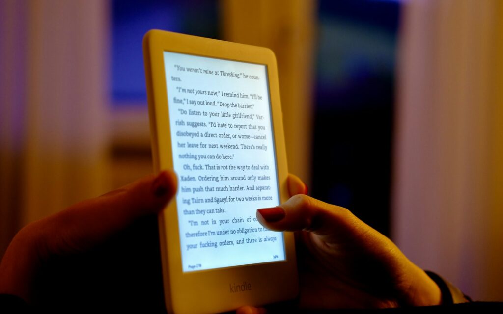 Lettore di ebook illuminato tenuto in mano in una stanza in penombra
